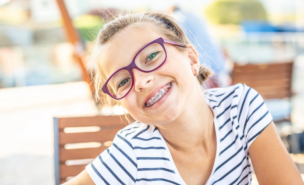 Image of child with braces wearing purple glasses smiling.