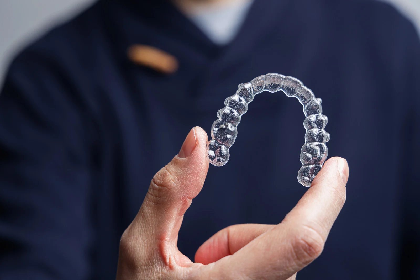 Hand holding clear aligner for invisible orthodontics teeth straightening treatment - MP Orthodontics